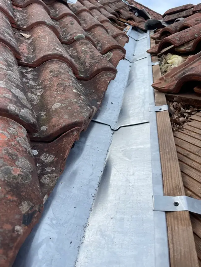 Noue en zinc fraîchement posée entre deux pans de toiture en tuiles